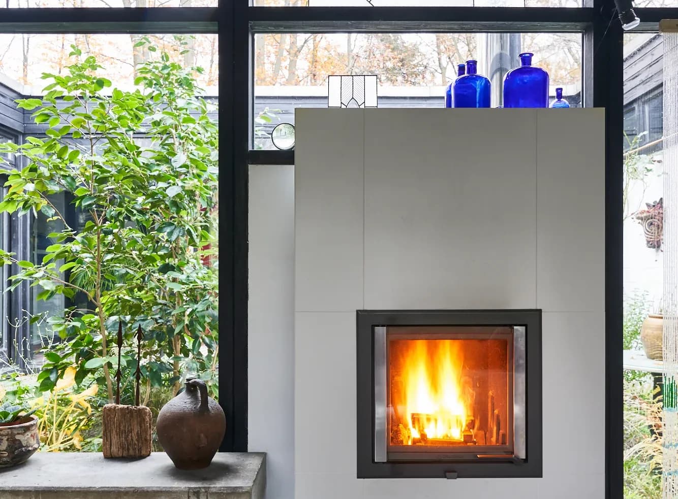 Weiß verputzter Speicherofen mit brennendem Feuer in einem verglasten Wintergarten